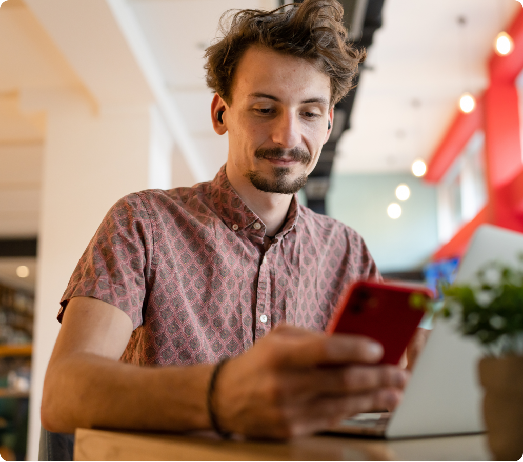 young man sitting at a desk checking his smartphone while working